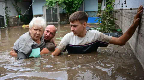 Getty Images Local residents rescue an elderly man (C) from the rising flood waters in the Romanian village of Slobozia Conachi, 14 September 2024.